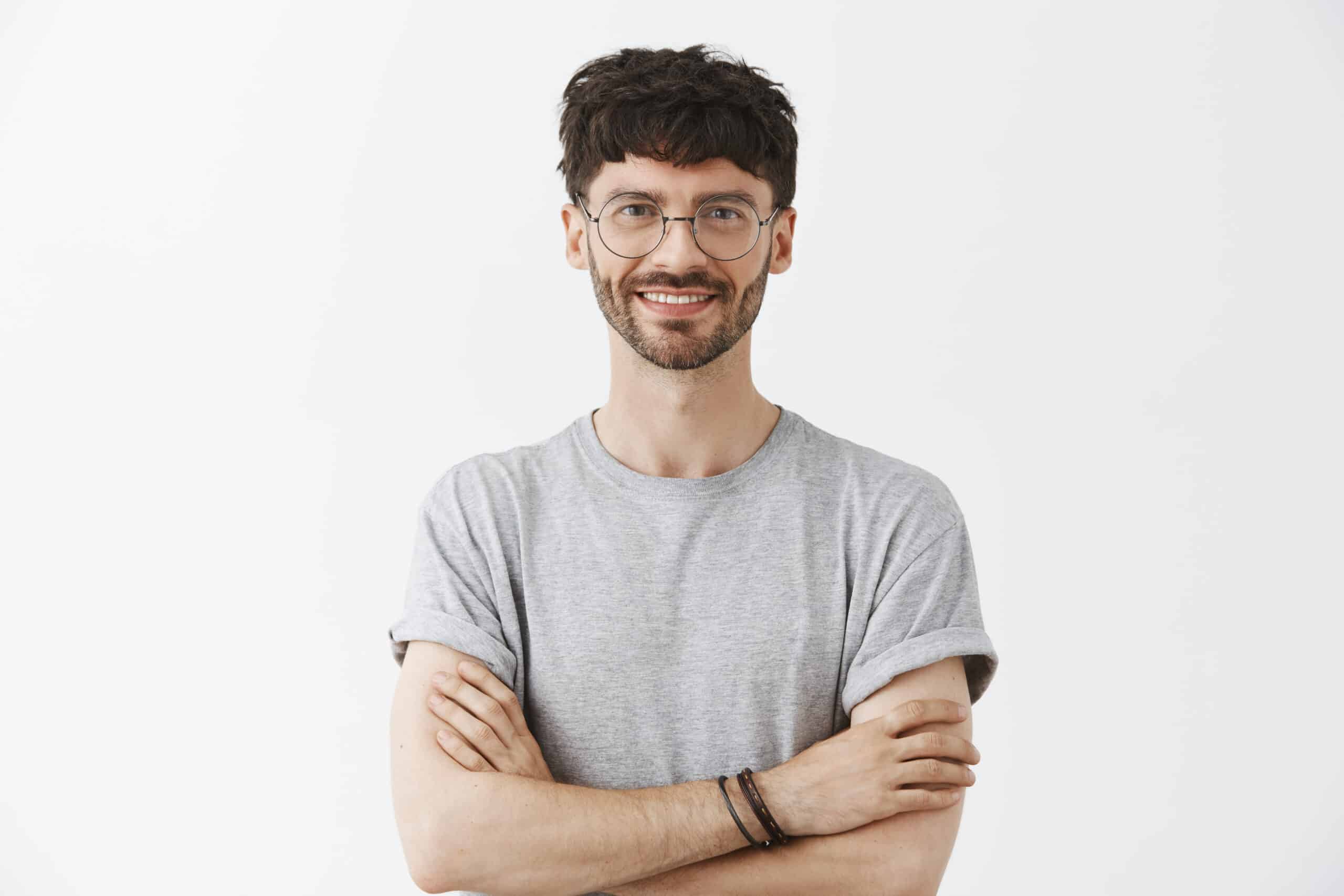 Waist up shot of pleased and creative satisfied male entrepreneur in transparent glasses holding hands crossed on chest in self assured pose smiling joyfully answering on questions of students